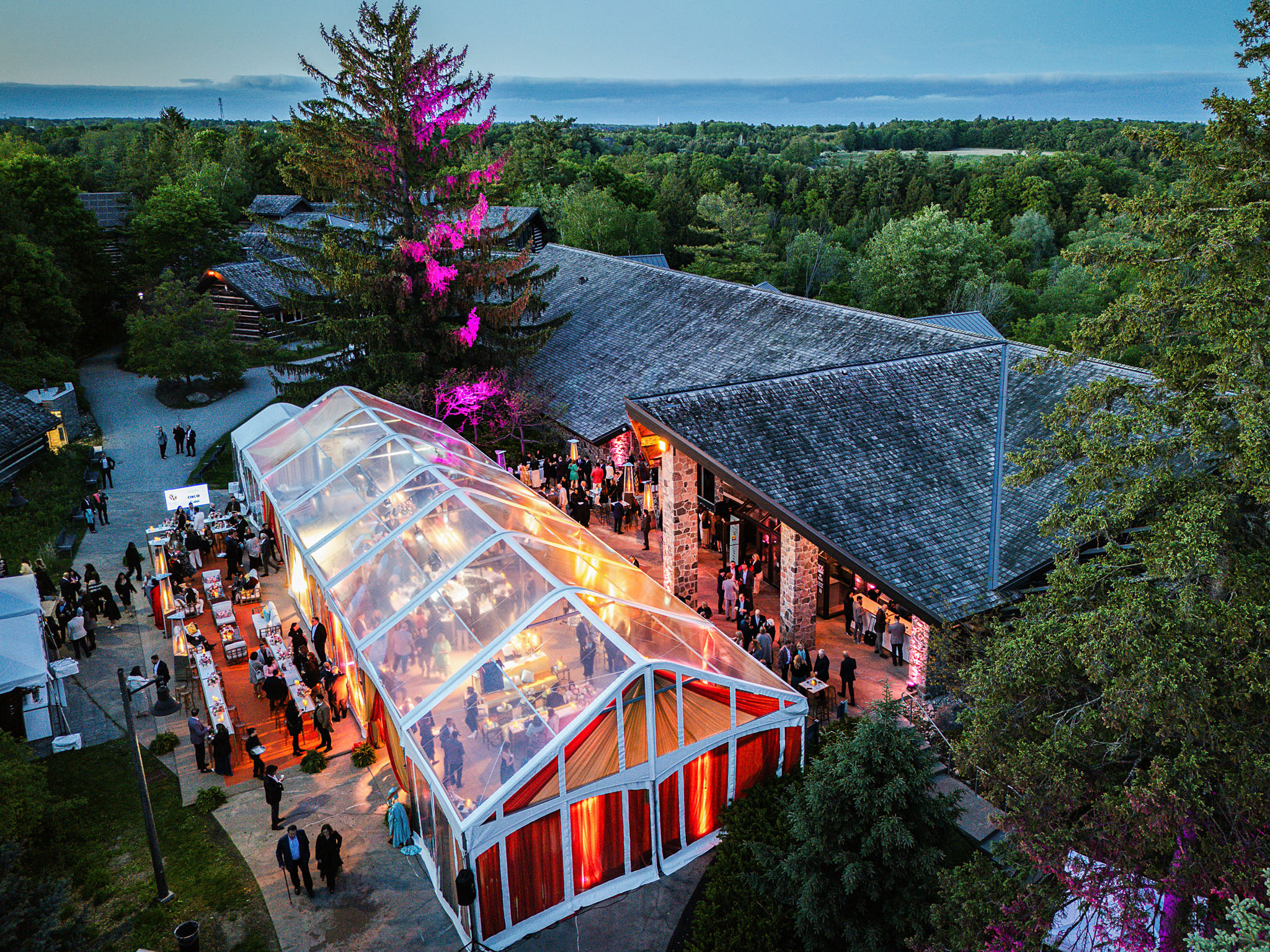 Aerial view of a plexiglass pavilion lit at night among trees.