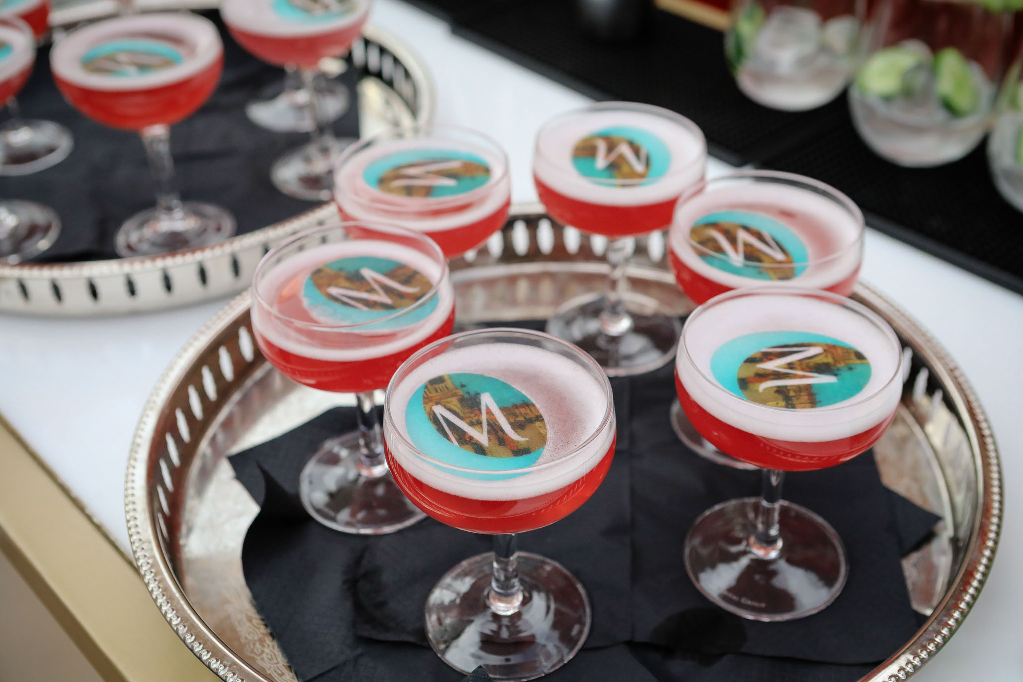 Tray of pink cocktails in coupe glasses with decorative monogram toppers.